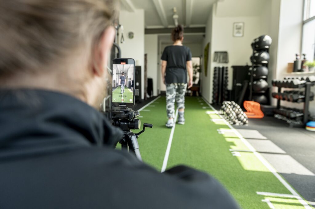 Bewegungsanalyse im Personal Training in Mönchengladbach: Ein Smartphone auf einem Stativ filmt eine Kundin beim Gehen über die Kunstrasenbahn.