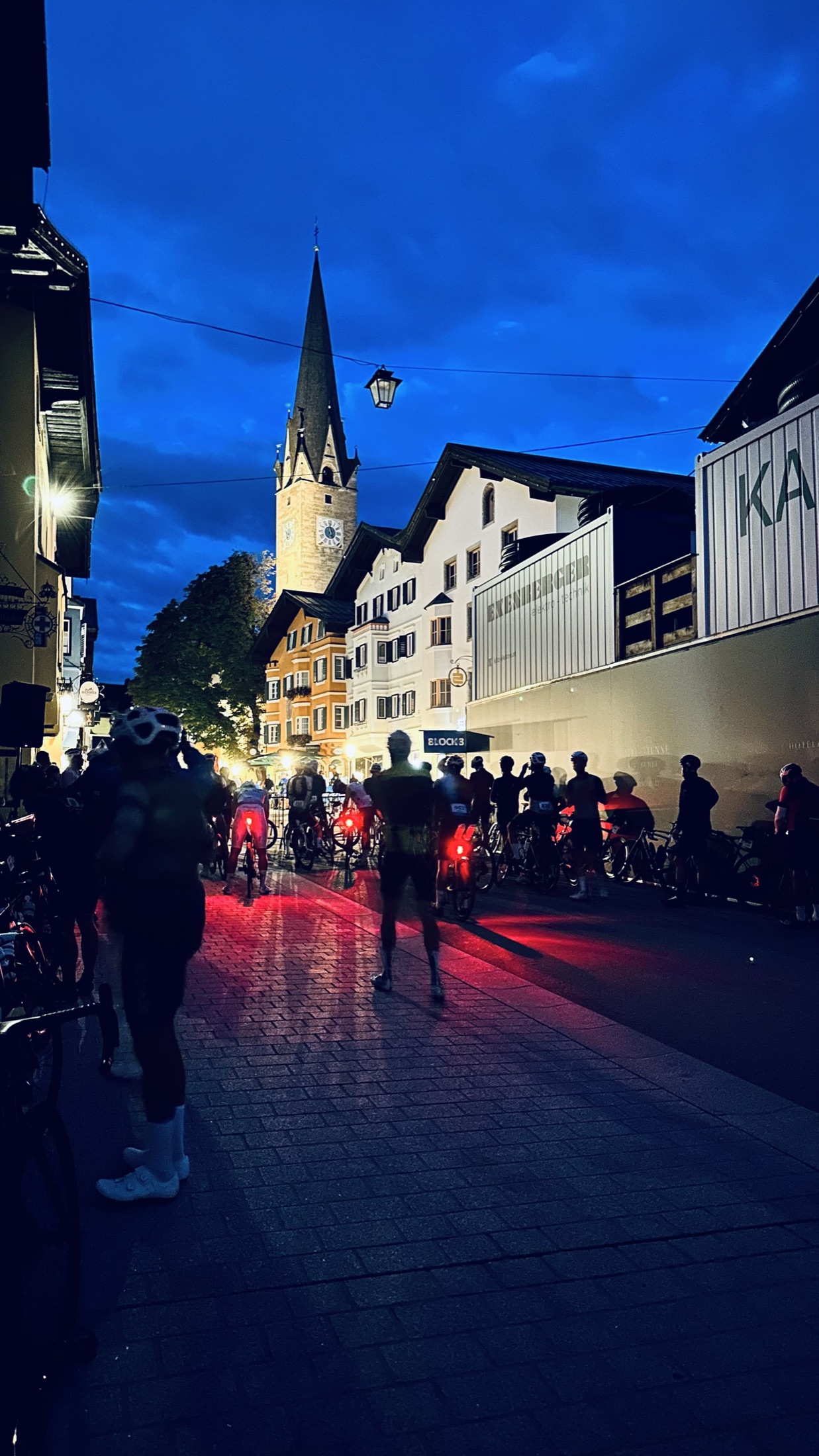 Radfahrer warten bei blauem Morgenlicht in der beleuchteten Kitzbüheler Innenstadt.