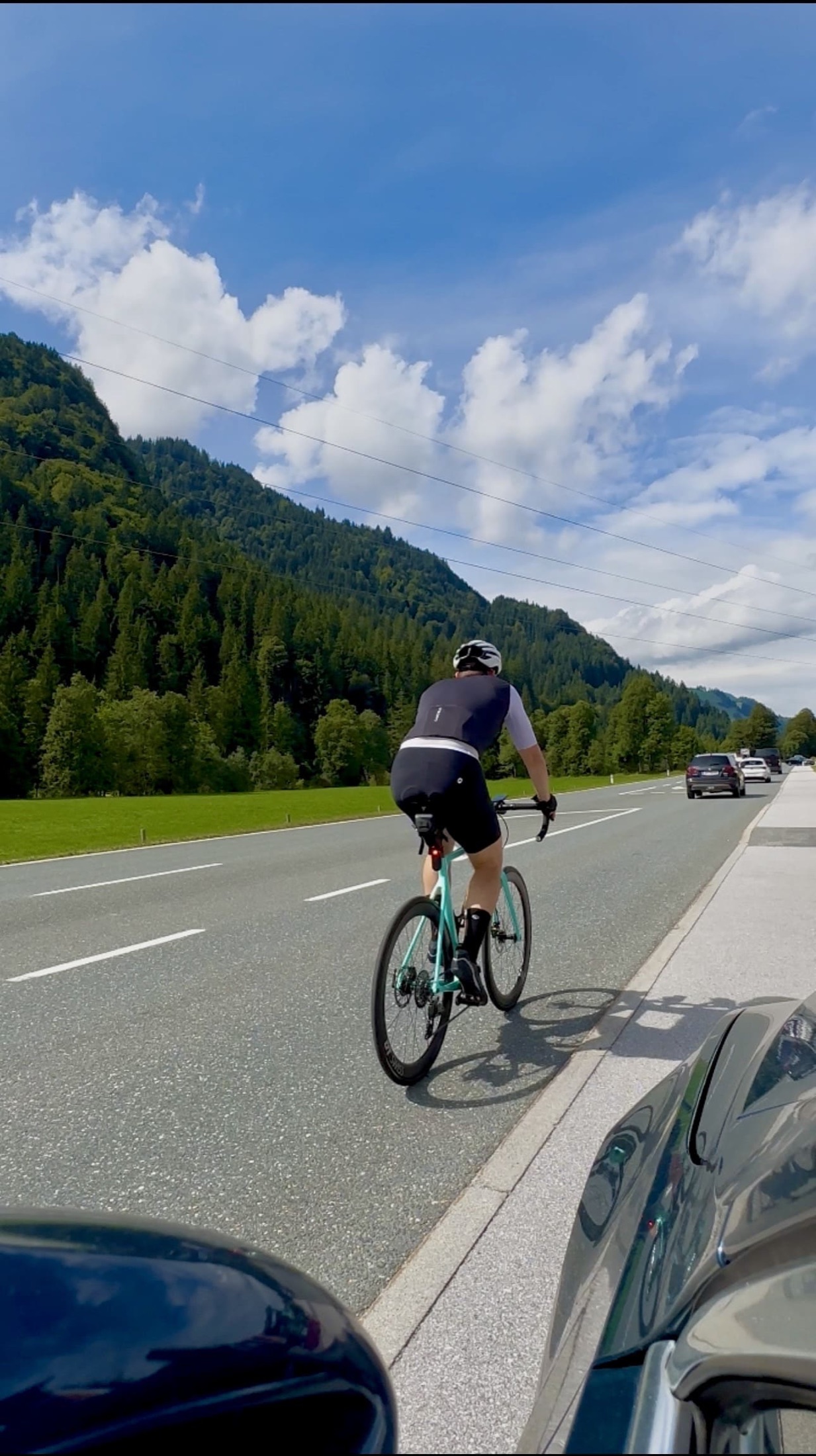 Christian fährt auf seinem türkisfarbenen Rennrad durch ein Tal mit bewaldeten Bergen.