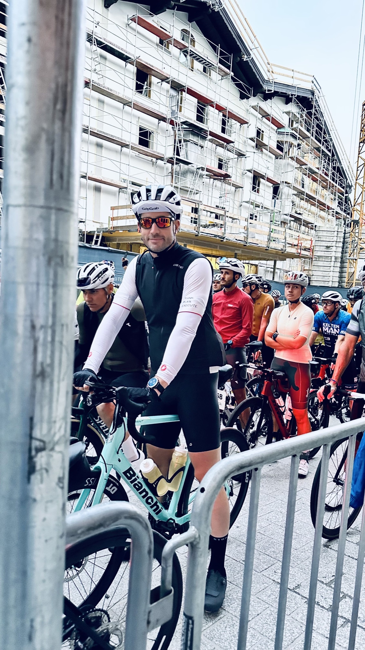 Christian wartet mit Helm, Sportbrille und türkisfarbenem Rennrad hinter einer Absperrung.